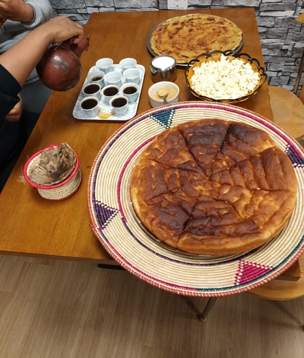 A wooden table laid for an Ethiopian coffee ceremony, with a woven mesob basket of sliced flatbread, bowls of popcorn and roasted grain, a clay jebena pot and small cups.